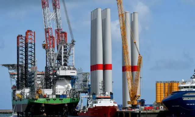 Un navire jack-up avec des grues massives se tient à côté de grandes tours d'éoliennes, prêt pour l'installation.