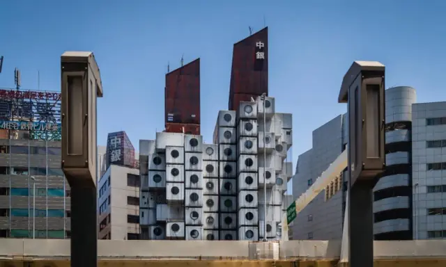 Iconica Nakagin Capsule Tower, un capolavoro di architettura modulare con capsule cubiche impilate, si staglia contro il cielo azzurro.