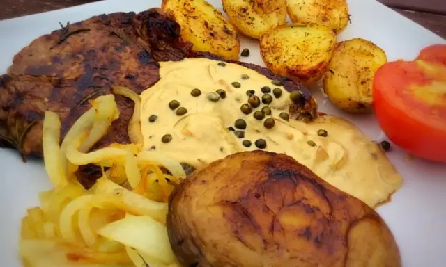 Stek z aromatycznym sosem z zielonego pieprzu, podany z pieczonymi ziemniakami, karmelizowaną cebulką i pomidorem.