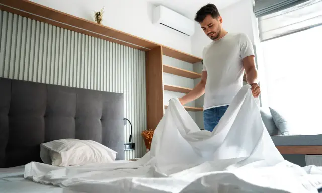 Hombre cambiando sábanas, un paso clave para saber como quitar acaros del colchon y mantener un ambiente fresco y saludable.