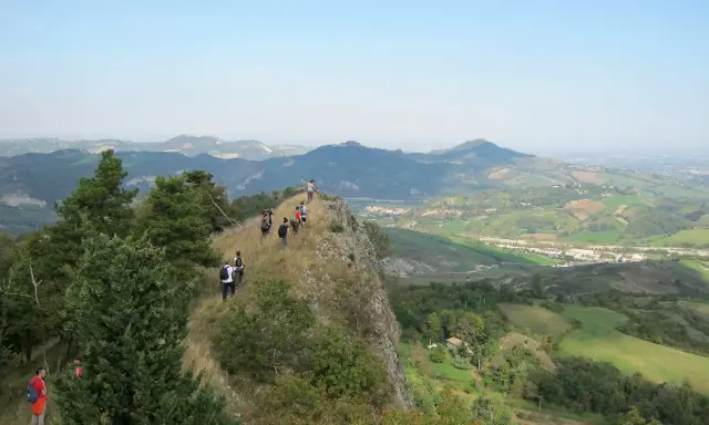 Un gruppo di escursionisti fa trekking su un crinale roccioso con vista panoramica sulle colline verdi, un'avventura indimenticabile vicino a Rimini.