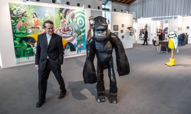 Mann in Anzug neben Gorilla-Skulptur auf Kunstmesse. Bunte Gemälde im Hintergrund zeigen aktuelle Kunst.