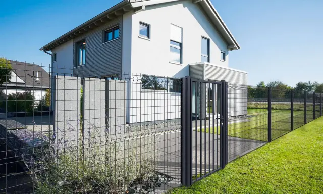Maison moderne avec portail et pose grillage rigide, délimitant un jardin verdoyant.