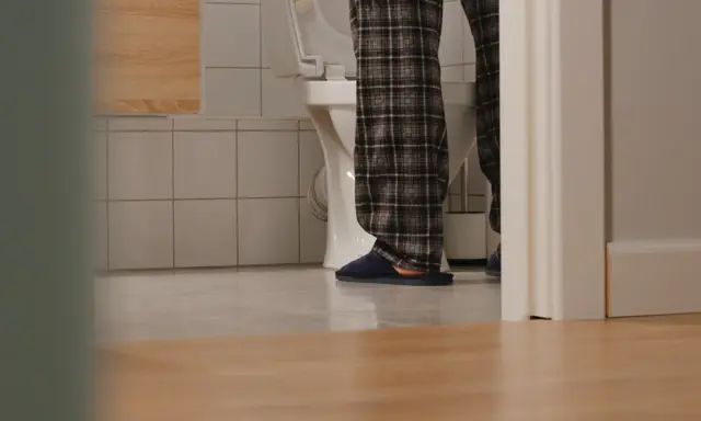 Osoba w piżamie stoi przy toalecie, doświadczając problemu z oddawaniem moczu.