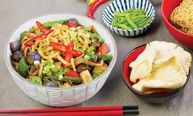 Pikantny makaron z tofu, bakłażanem, papryką i szczypiorkiem. Obok miseczki z fasolką szparagową i grzybami.