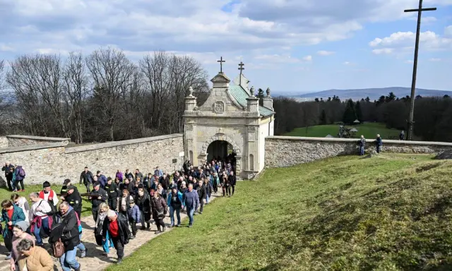 Pielgrzymka wchodzi przez zabytkową bramę. W oddali widać krzyż i piękne krajobrazy, które są nowa słupia atrakcje.