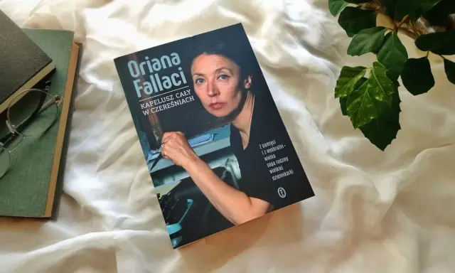 Książka "Kapelusz cały w czereśniach" Oriany Fallaci leży obok okularów i innych książek.