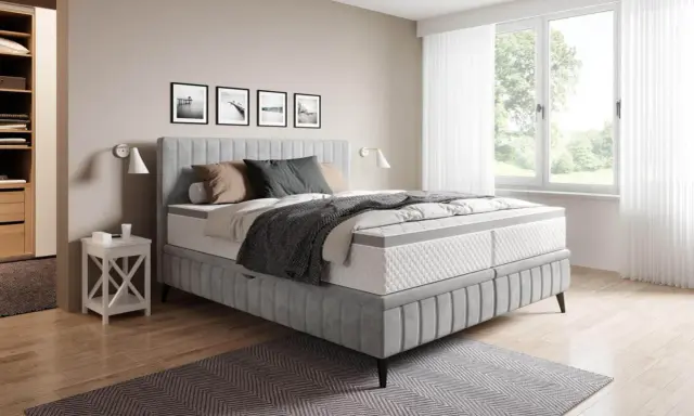 Sovrum med en stor säng i grått tyg. En fin balans att blanda beige och grått inredning med detaljer i trä och svarta tavlor på väggen.