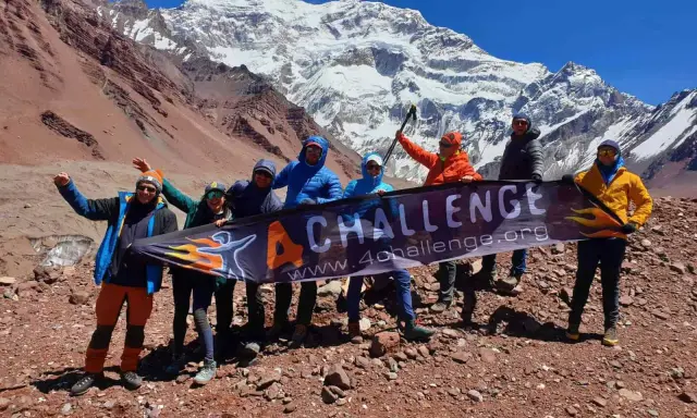 Grupa zdobywców z banerem "4 CHALLENGE" na tle majestatycznych gór z Aconcagua.