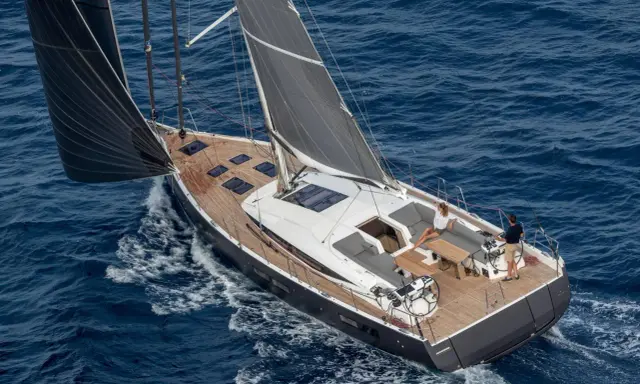 Un couple profite d'une croisière sur un voilier habitable à l'année, naviguant sur des eaux bleues par une journée ensoleillée.