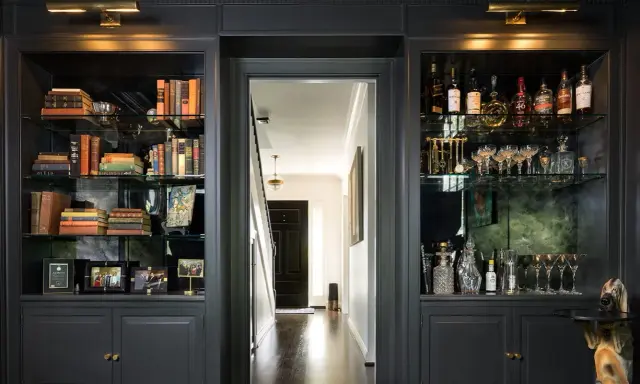 Estanterías oscuras con libros, botellas y copas. Ideas para como decorar una libreria con estilo y elegancia.