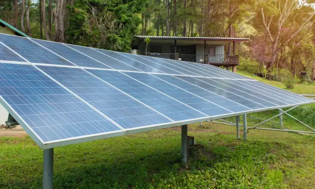 Grandes panneaux solaires au sol, installés dans un jardin verdoyant, captent l'énergie du soleil pour alimenter une maisonnette en bois.