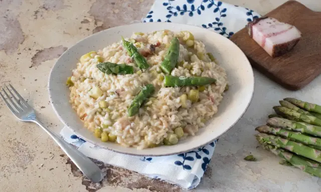 Un cremoso risotto con asparagi e pancetta, guarnito con punte di asparagi freschi e una spolverata di parmigiano.