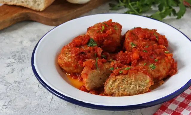 Polpette di pane succulente in salsa di pomodoro, guarnite con prezzemolo fresco. Un piatto casalingo che profuma di tradizione.