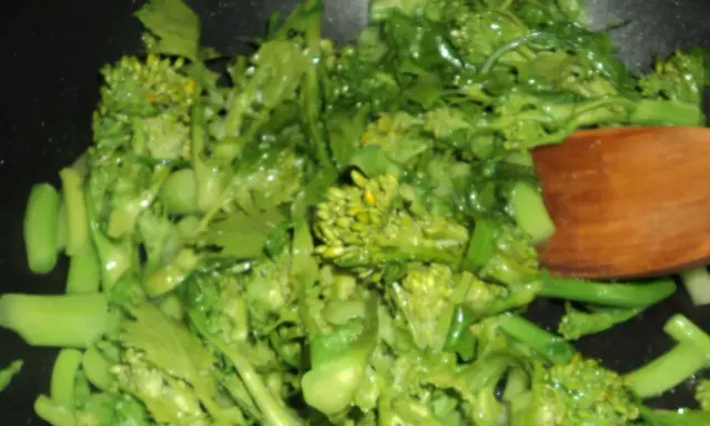 Cime di rapa salteados en sartén con una cuchara de madera. Verduras verdes vibrantes y frescas, listas para ser disfrutadas.