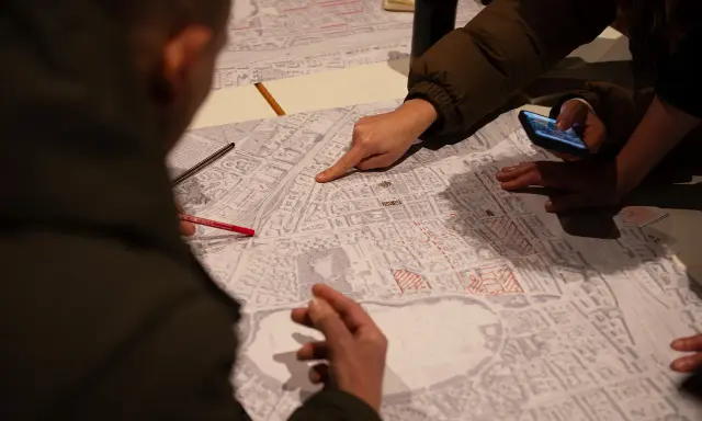 Menschen diskutieren auf einer Karte, die Details der Stadt zeigt. Sie planen die monitoring soziale stadtentwicklung, markieren Bereiche und nutzen ein Smartphone.