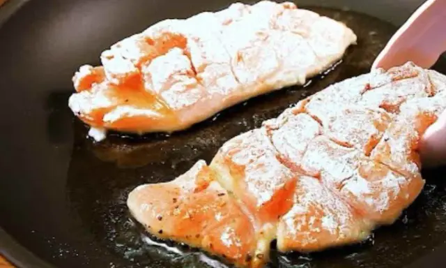 Due filetti di petto di pollo infarinati cuociono in padella, sfrigolando nell'olio caldo.