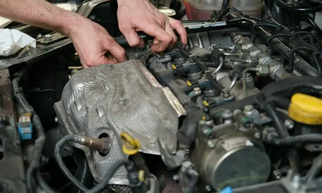 Mechanik pracuje przy silniku, wymieniając czujnik położenia wałka rozrządu.
