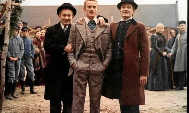 Trzech mężczyzn w eleganckich strojach, otoczonych tłumem, jakby w drodze do ziemi obiecanej.