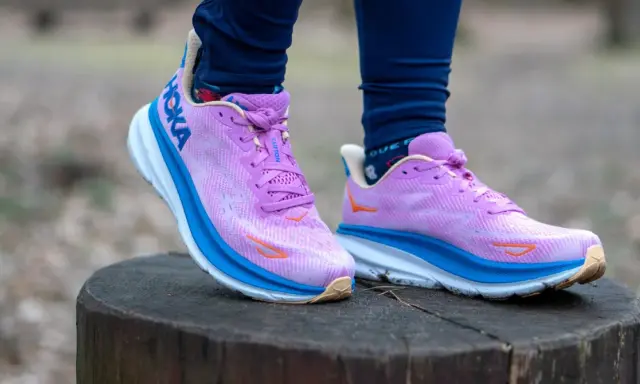 Fioletowe buty Hoka Clifton na pniu drzewa. Hoka to firma znana z amortyzacji.