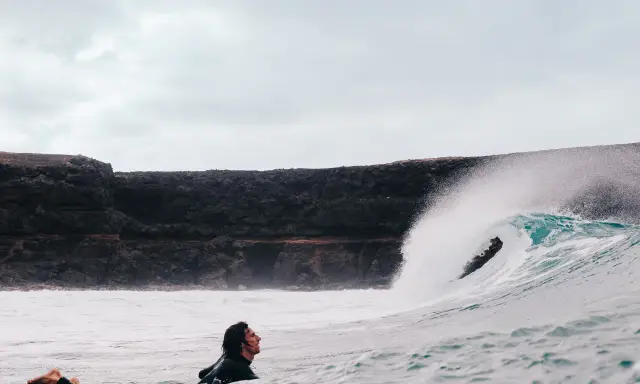Surfer wartet auf die perfekte Welle vor einer Felswand, um Costa Calma surfen zu gehen.