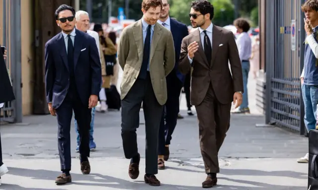 Trzech mężczyzn w eleganckich garniturach i stylowych loafersach do garnituru idzie ulicą.