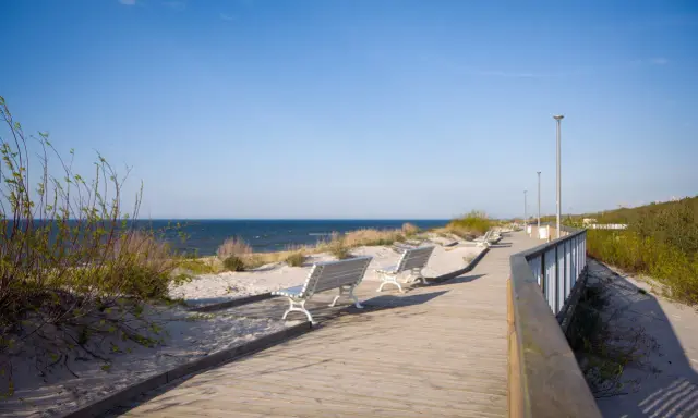 Drewniana promenada w Dziwnowie z ławkami i widokiem na morze. Idealne miejsce na spacer i podziwianie atrakcji nadmorskich.