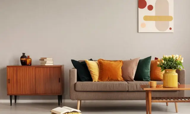 Un salon cosy aux couleurs automnales, avec un canapé garni de coussins ocre et vert forêt, un meuble vintage en bois et une peinture abstraite.