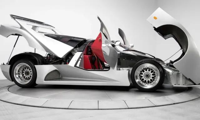 Silberner Lotec C1000 Supersportwagen mit geöffneten Türen und Hauben, rote Sitze und sichtbarer Motor.