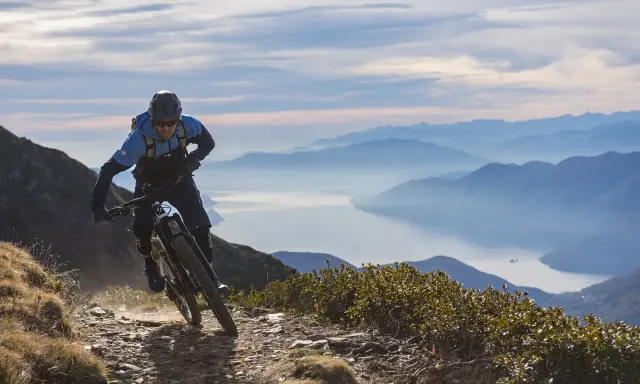 Ein Mountainbiker auf einer abenteuerlichen Tour in den Alpen, mit einem See und Bergketten im Hintergrund.
