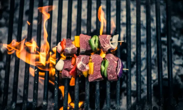 Brochetas de carne y verduras sobre parrilla de carbón, llamas naranjas. ¡Así se hace barbacoa carbón!