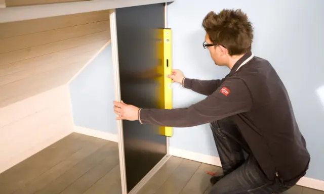 Un homme utilise un niveau pour fabriquer un placard sous pente de toit.