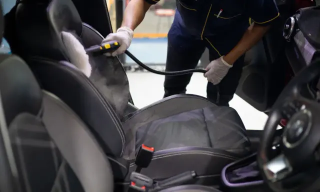 Un profesional usa vapor para limpiar los asientos del coche, mostrando cómo limpiar los asientos del coche de forma efectiva.