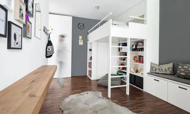 Ein weißes Hochbett mit integrierten Regalen und Stauraum bietet viele Ideen unterm Hochbett für Spielzeug und Bücher. Ein Holzbalken und ein Kuhfell-Teppich ergänzen den Raum.