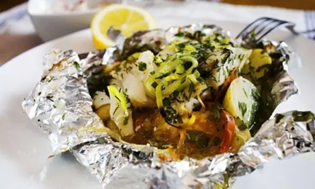 En läcker fiskpaket i ugn med potatis, tomat och örter, toppad med citron och purjolök. Enkel och smakrik middag.