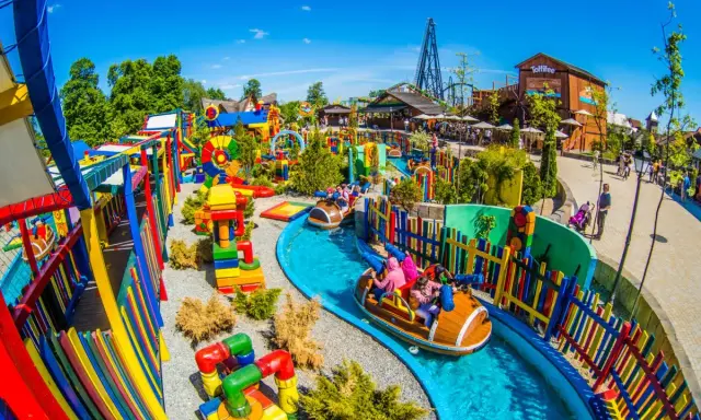 Parque acuático colorido con atracciones para niños en Cracovia. Barcas navegan por un río azul rodeado de juegos y vallas vibrantes.