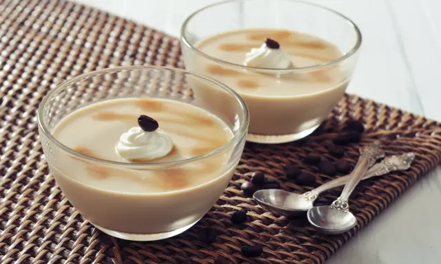 Deux coupes de **dessert au café** onctueux, garnies de crème fouettée et d'un grain de café, sur un napperon tressé.