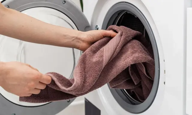 Manos colocando una toalla rosa en una lavadora. Aprende como lavar toallas para que queden suaves y esponjosas.