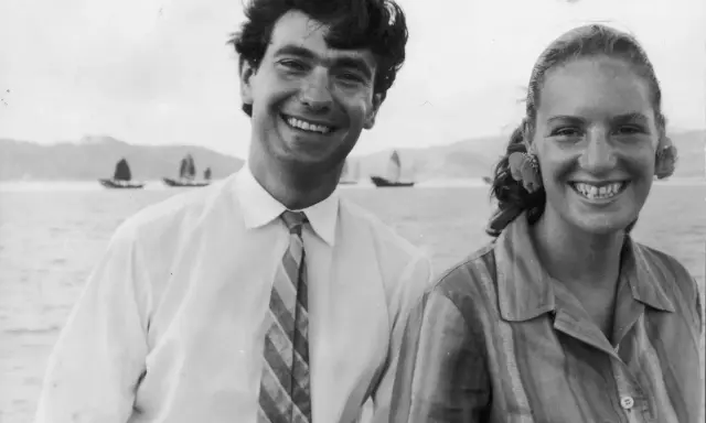 Angela Staude sorride con un uomo su una barca, con velieri sullo sfondo.