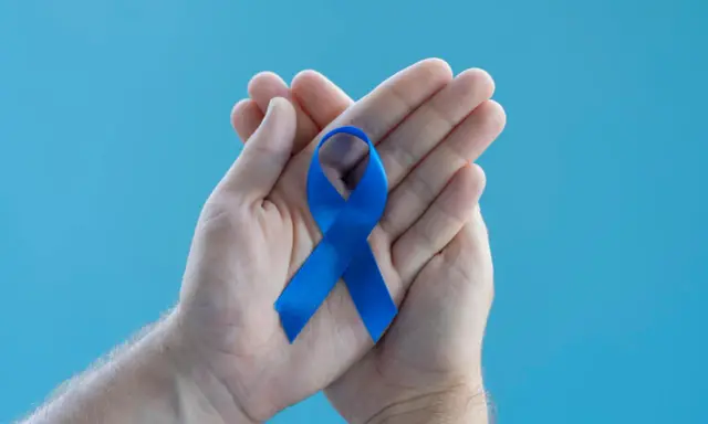 Dłonie trzymające niebieską wstążkę symbolizującą wsparcie dla mężczyzn. Warto poznać domowe sposoby na prostatę.