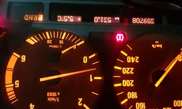 Czerwony wykrzyknik BMW świeci się na desce rozdzielczej, obok wskaźników prędkości i obrotów.