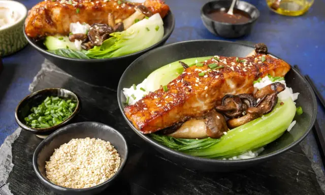 Två skålar med ris, bok choy, svamp och glaserad sous vide lax, toppad med sesamfrön och gräslök.