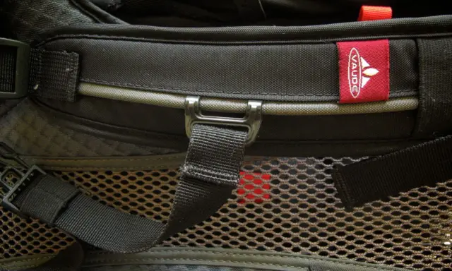 Czerwona metka z logo **Vaude** na czarnym plecaku. Firma Vaude to niemiecki producent sprzętu turystycznego.