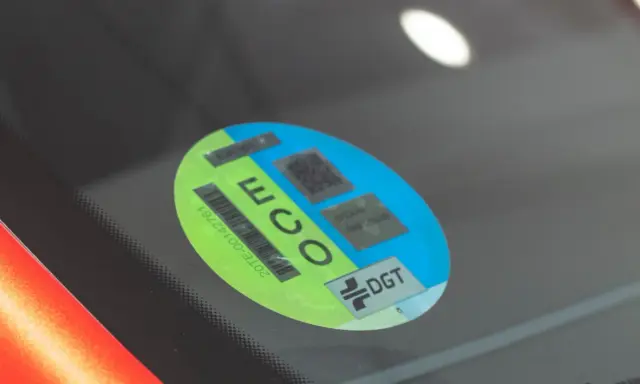 Mini etiqueta eco en parabrisas. Muestra el distintivo DGT y códigos QR para identificar vehículos de bajas emisiones.