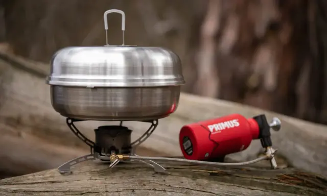 En primus kaffepanna på en campingkök med en röd gasbehållare. Perfekt för fika i naturen.