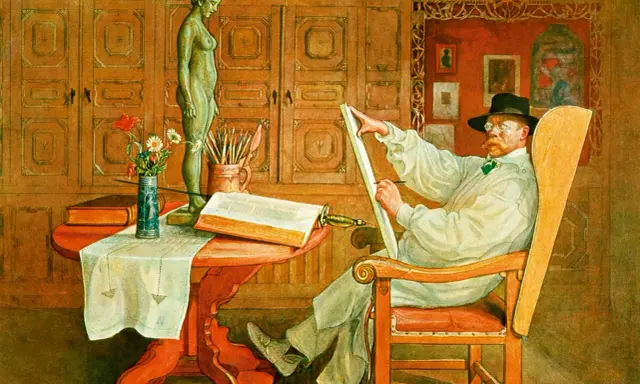 Carl Larsson sitter i en stol och ritar på en duk. Framför honom står en statyett, en bok och en vas med blommor.
