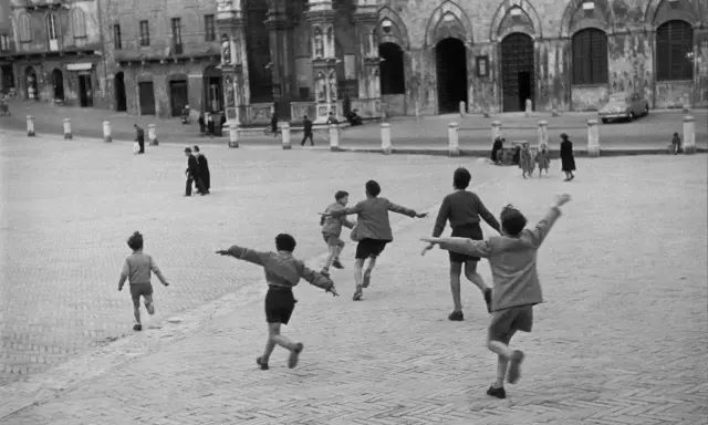Bambini corrono in una piazza storica, un'immagine piena di movimento e gioia, perfetta come idee per foto.