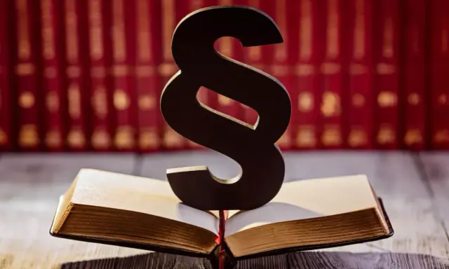 Symbol paragrafu na otwartej księdze, sugerujący karę finansową dla pracownika. W tle rząd czerwonych ksiąg.