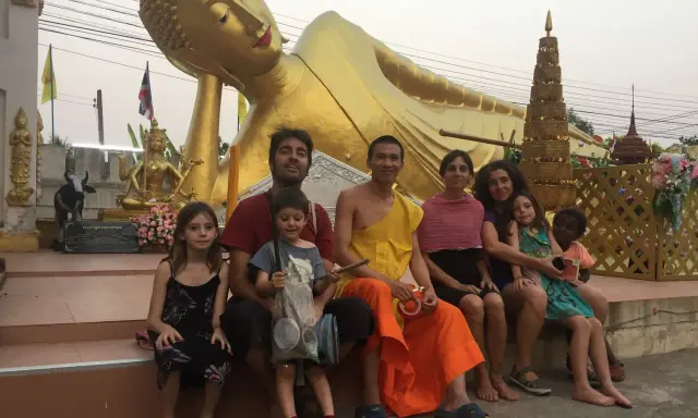 Familia disfrutando de un viaje a Asia con niños, sentados frente a una estatua dorada de Buda reclinado.
