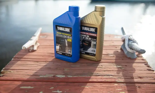 Deux bidons d'huile Yamalube pour moteur 4 temps, l'un bleu (10W-30) et l'autre doré (5W-30), sur un ponton en bois.